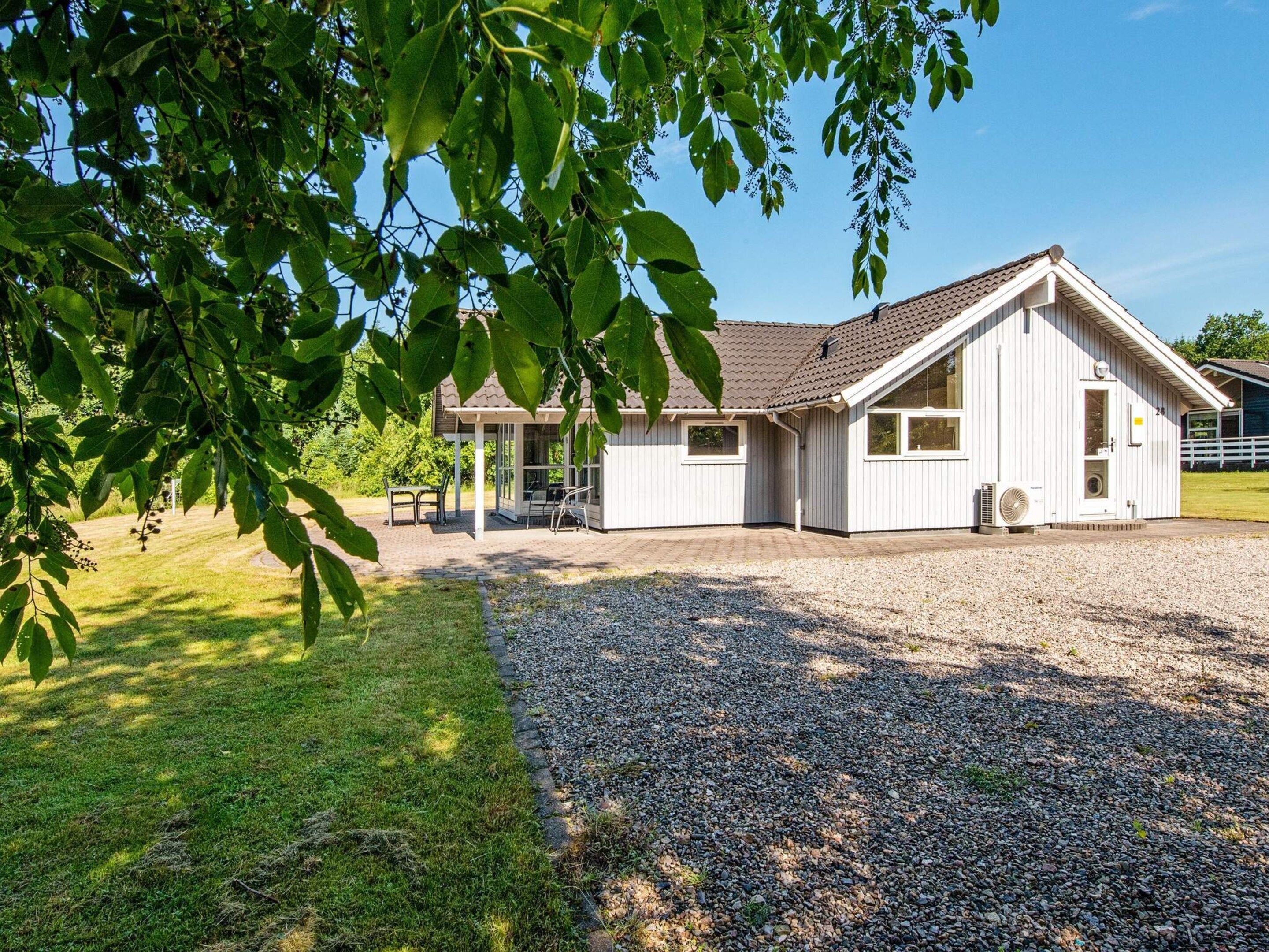 A white building with a sloped roof, a covered patio area, and a gravel driveway.