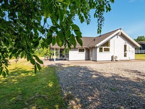 A white building with a sloped roof, a covered patio area, and a gravel driveway.