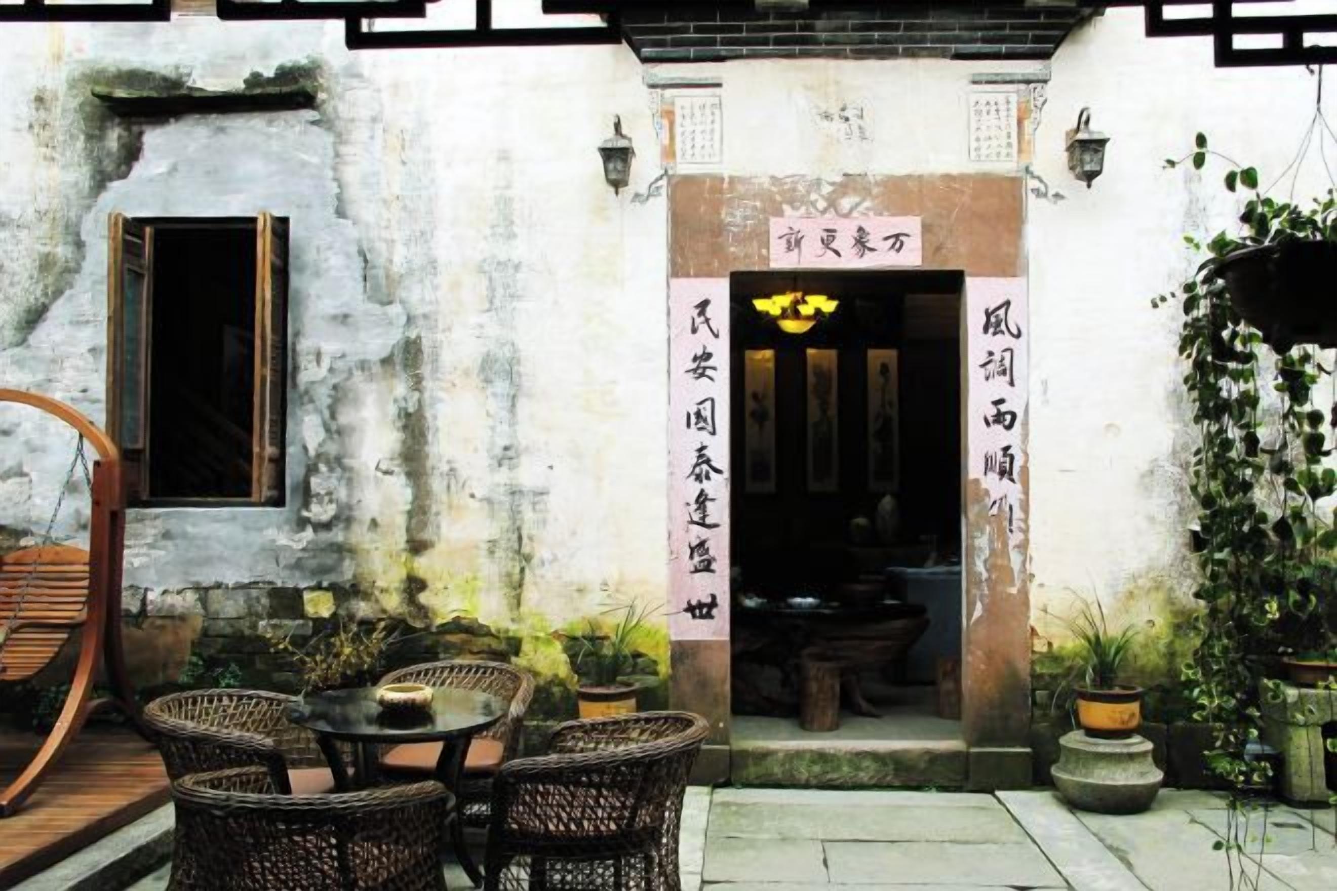 A traditional Chinese courtyard with a wooden door, wicker furniture, and potted plants.