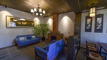 A room with a blue sofa, a wooden ceiling, a chandelier, and framed artwork on the walls.