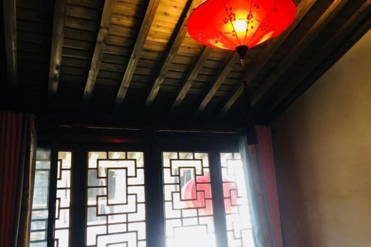 A room with wooden beams on the ceiling, a red lantern hanging, and a window with a geometric pattern.