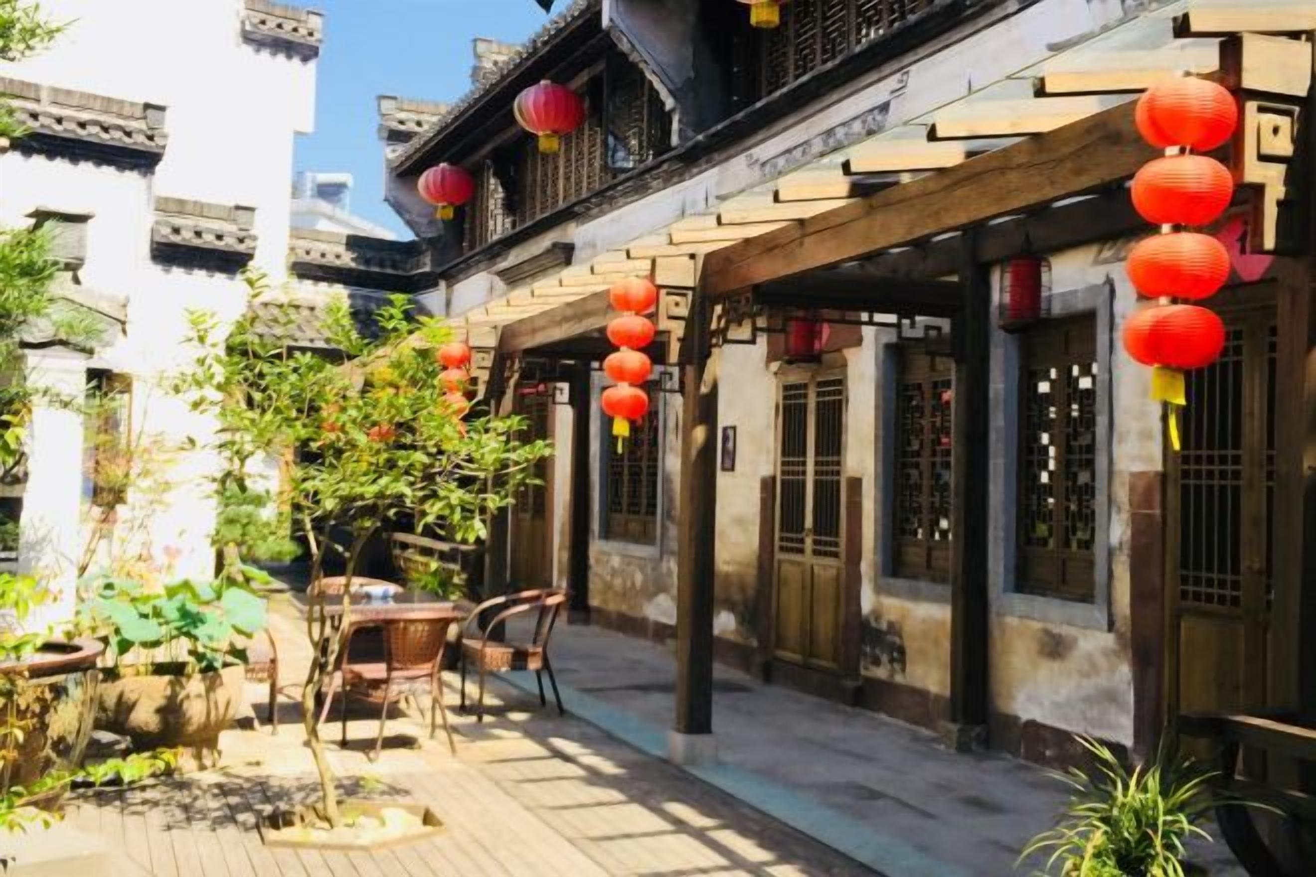 A courtyard with traditional architecture, including tiled roofs and wooden beams, and red lanterns hanging above.