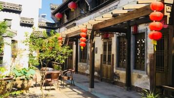 A courtyard with traditional architecture, including tiled roofs and wooden beams, and red lanterns hanging above.