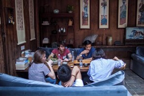 Un groupe de personnes est assis autour d’une table en bois dans une pièce au décor traditionnel, comprenant un canapé et des étagères fixées au mur.