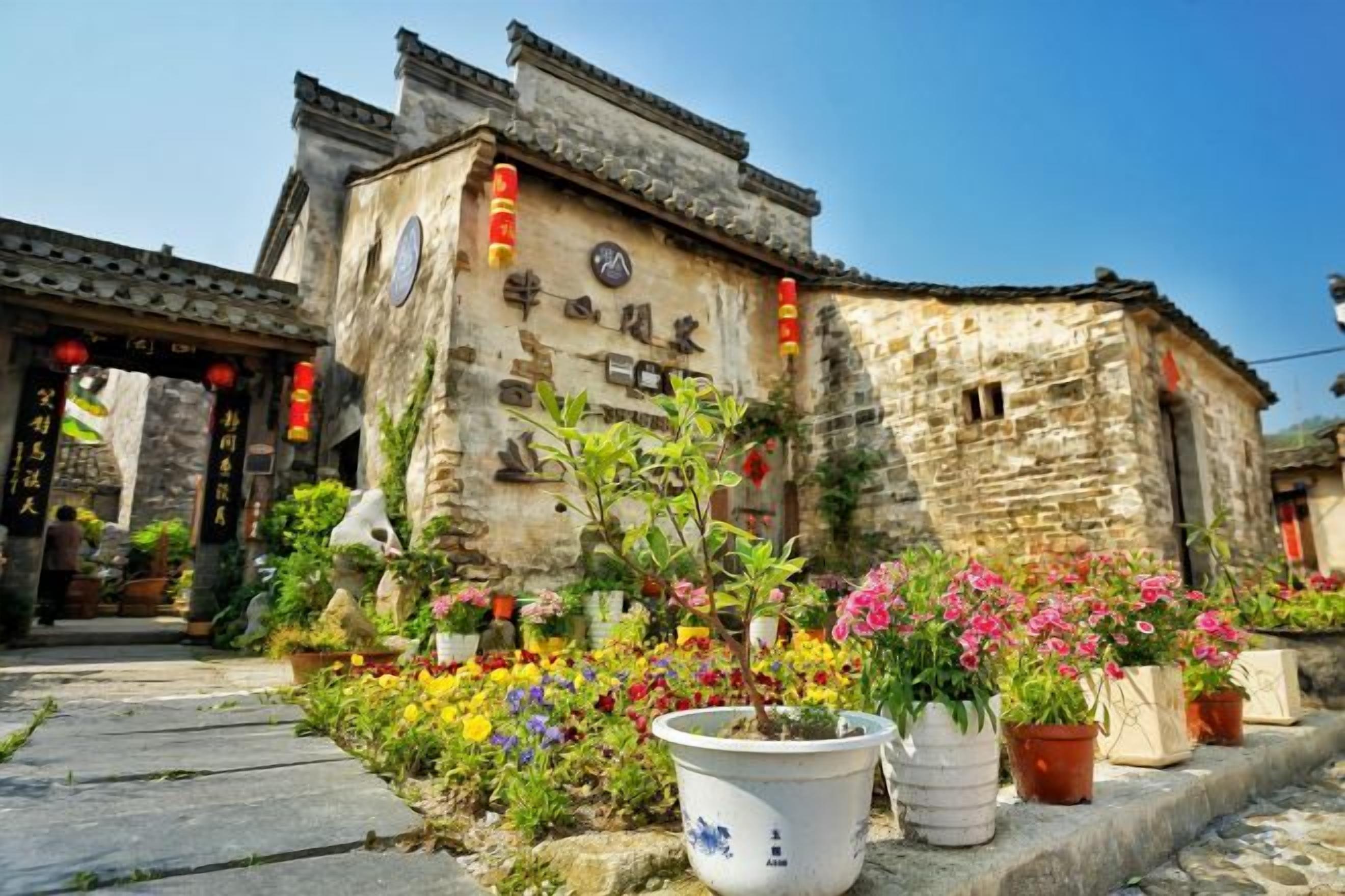 Un bâtiment traditionnel avec un toit en tuiles et une façade en pierre, entouré de plantes et de fleurs en pot.