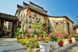 A traditional building with a tiled roof and a stone facade, surrounded by potted plants and flowers. - Banshan Xianke Inn (Huangshan City)