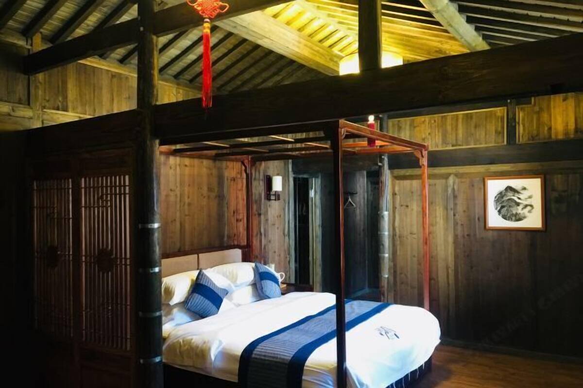 A wooden room with a four-poster bed, a traditional Chinese door, and a framed picture on the wall.