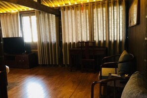 A room with wooden flooring, a television on a wooden cabinet, a dining table with chairs, and a window with curtains. - Banshan Xianke Inn (Huangshan City)