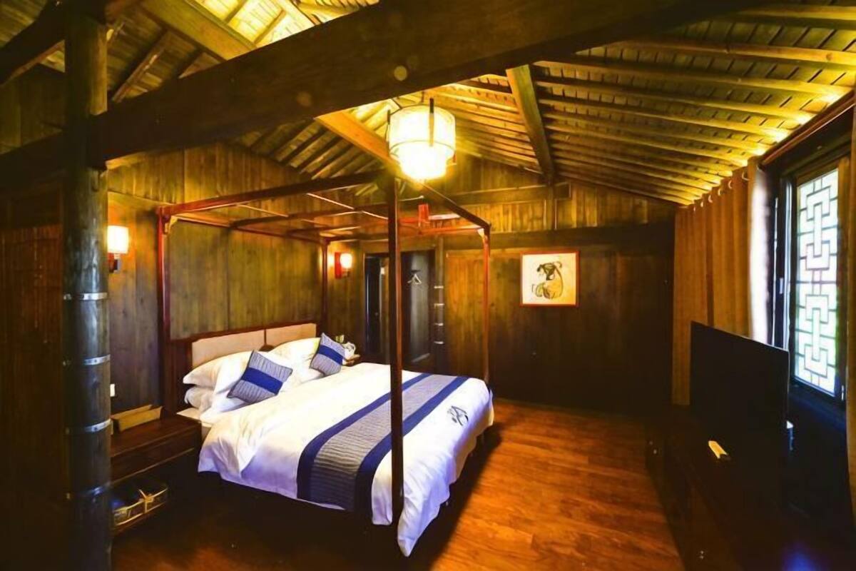 A four-poster bed in a wooden room with a sloped ceiling and a television on the right.
