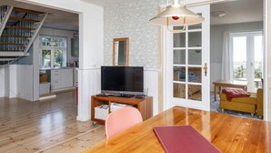 Un'ampia zona giorno con un tavolo da pranzo in legno, una televisione su un mobile e una scala che conduce a un piano superiore.