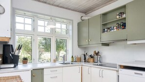 Una cucina con mobili bianchi, un piano di lavoro in legno, un lavello e una finestra con vista sul verde.