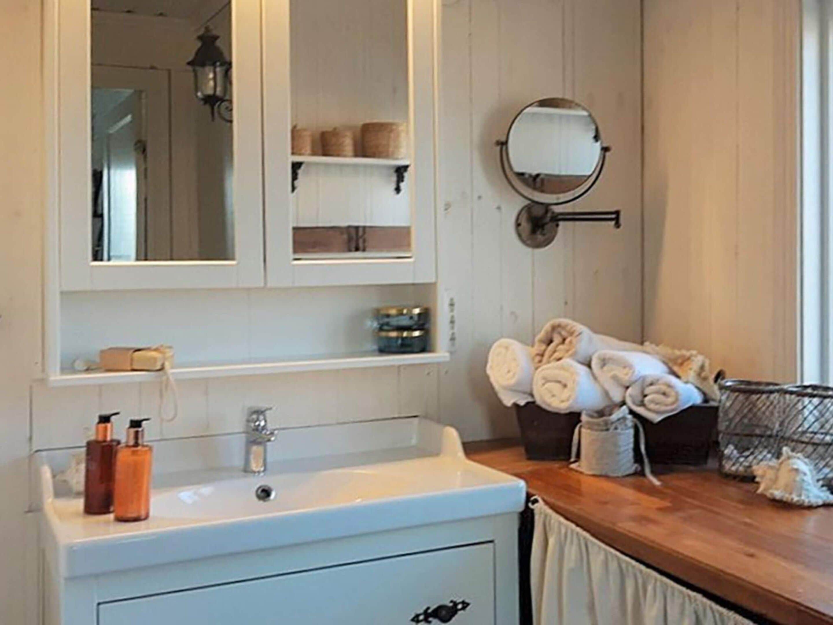 Et badeværelse med en hvid vask, et spejl og et håndklædestativ med håndklæder.
