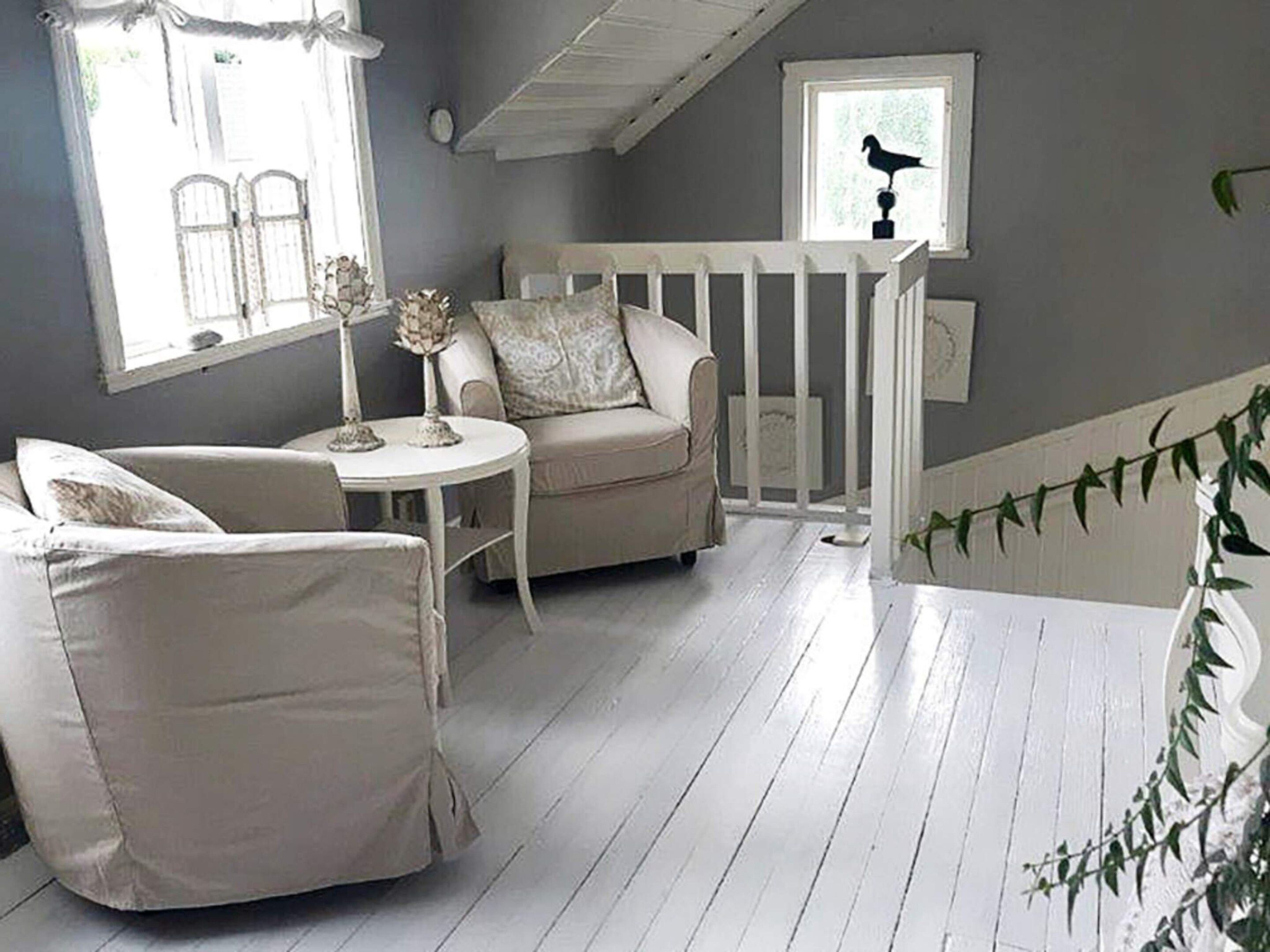 A room with a white wooden floor, a white chair, a small round table, and a white railing.