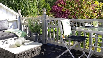 A deck with a sofa, a small table, and a chair. There are potted plants and a railing.