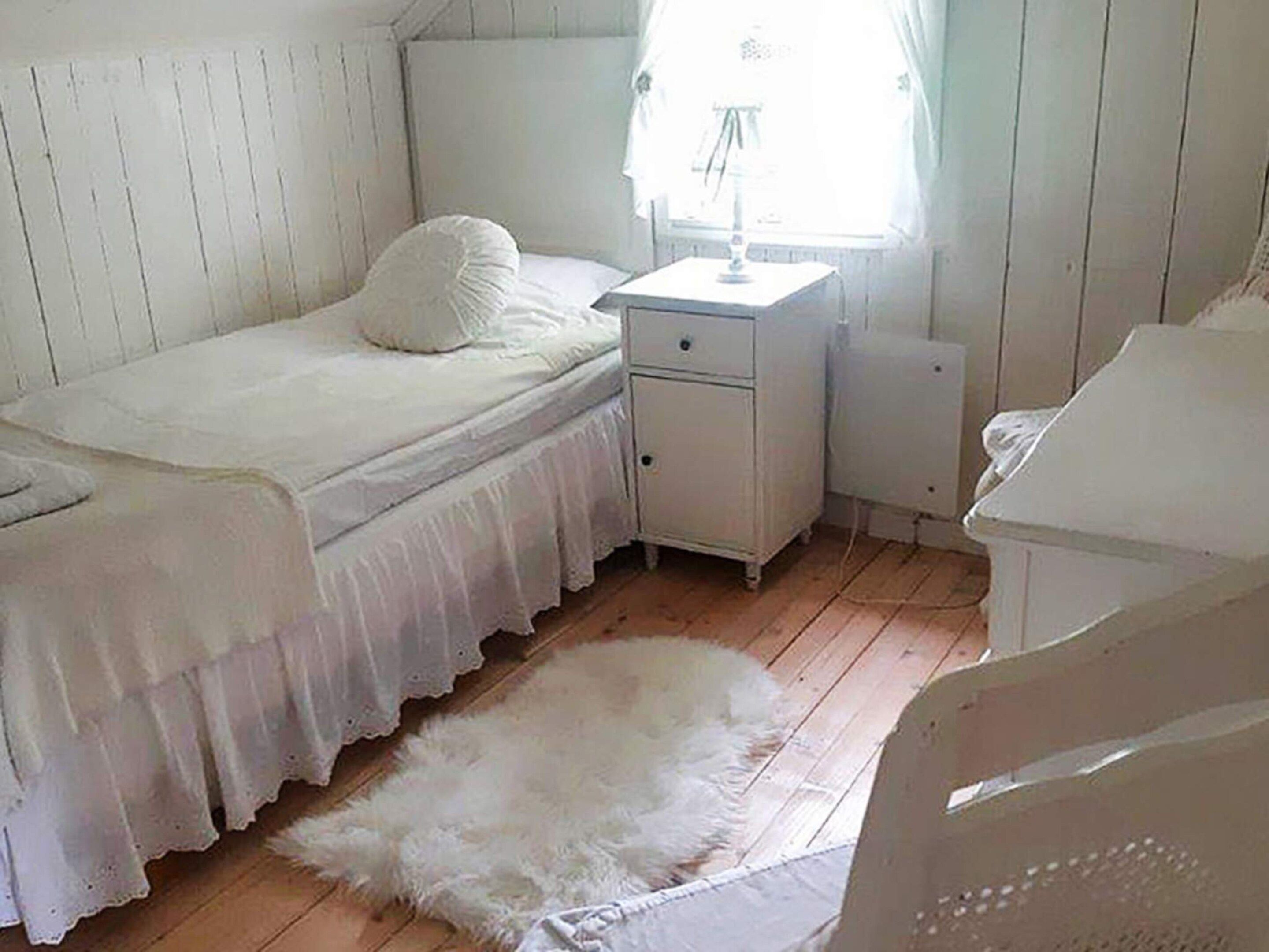 A bedroom with a single bed, a nightstand, a lamp, and a white furry rug on the floor.