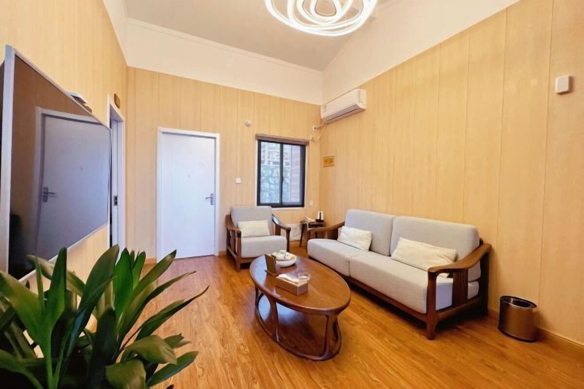 A modern living room with a wooden floor, a sofa, two armchairs, a coffee table, and a large window.