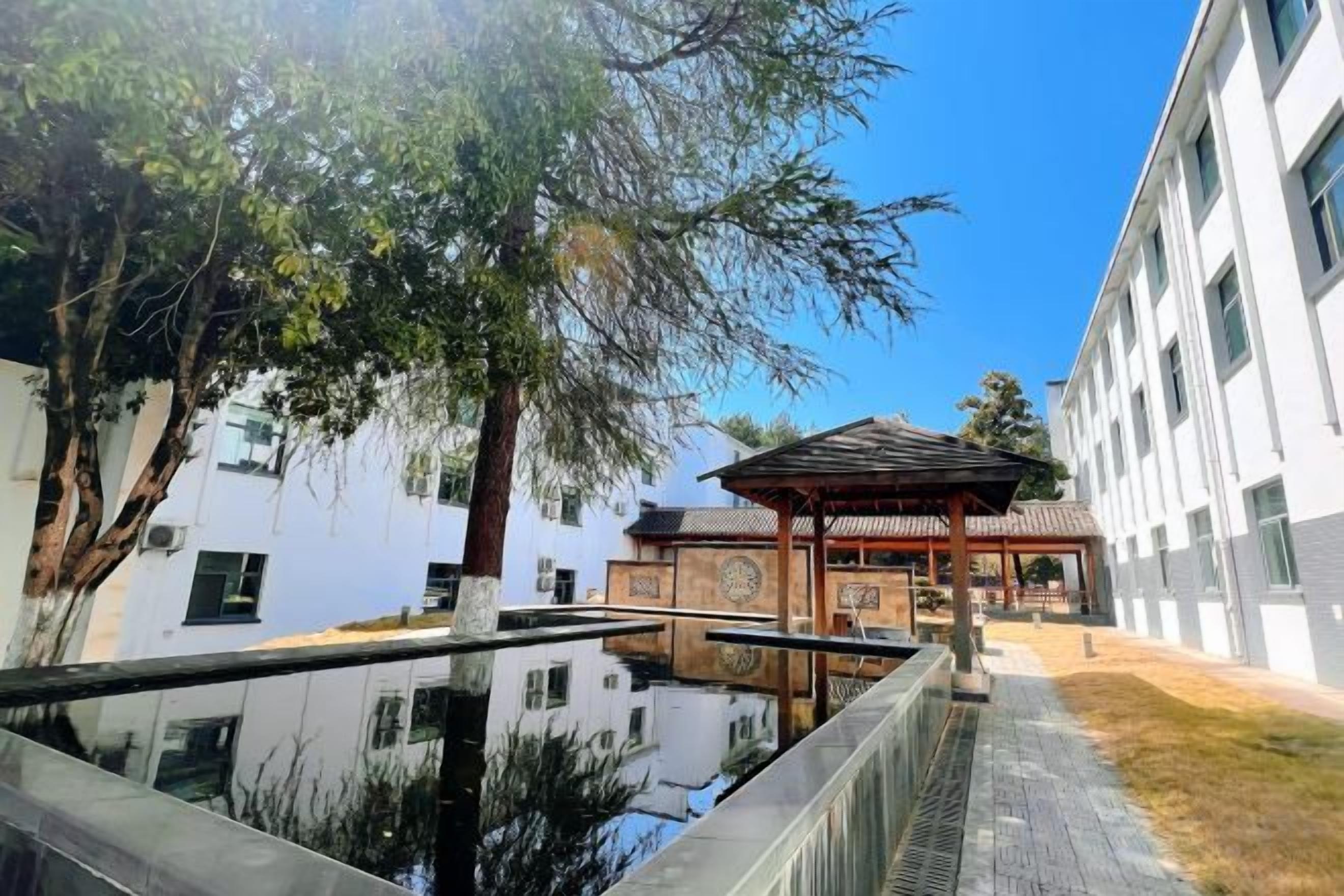 A courtyard with a traditional pavilion, a water feature, and modern buildings in the background.