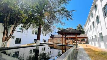 A courtyard with a traditional pavilion, a water feature, and modern buildings in the background.