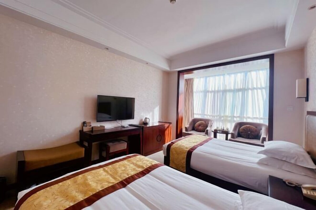 A hotel room with two beds, a TV, a desk, and a large window.
