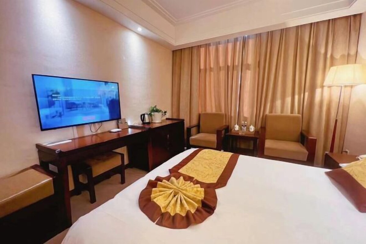 A hotel room with a bed, a desk, a television, a chair, and a lamp.