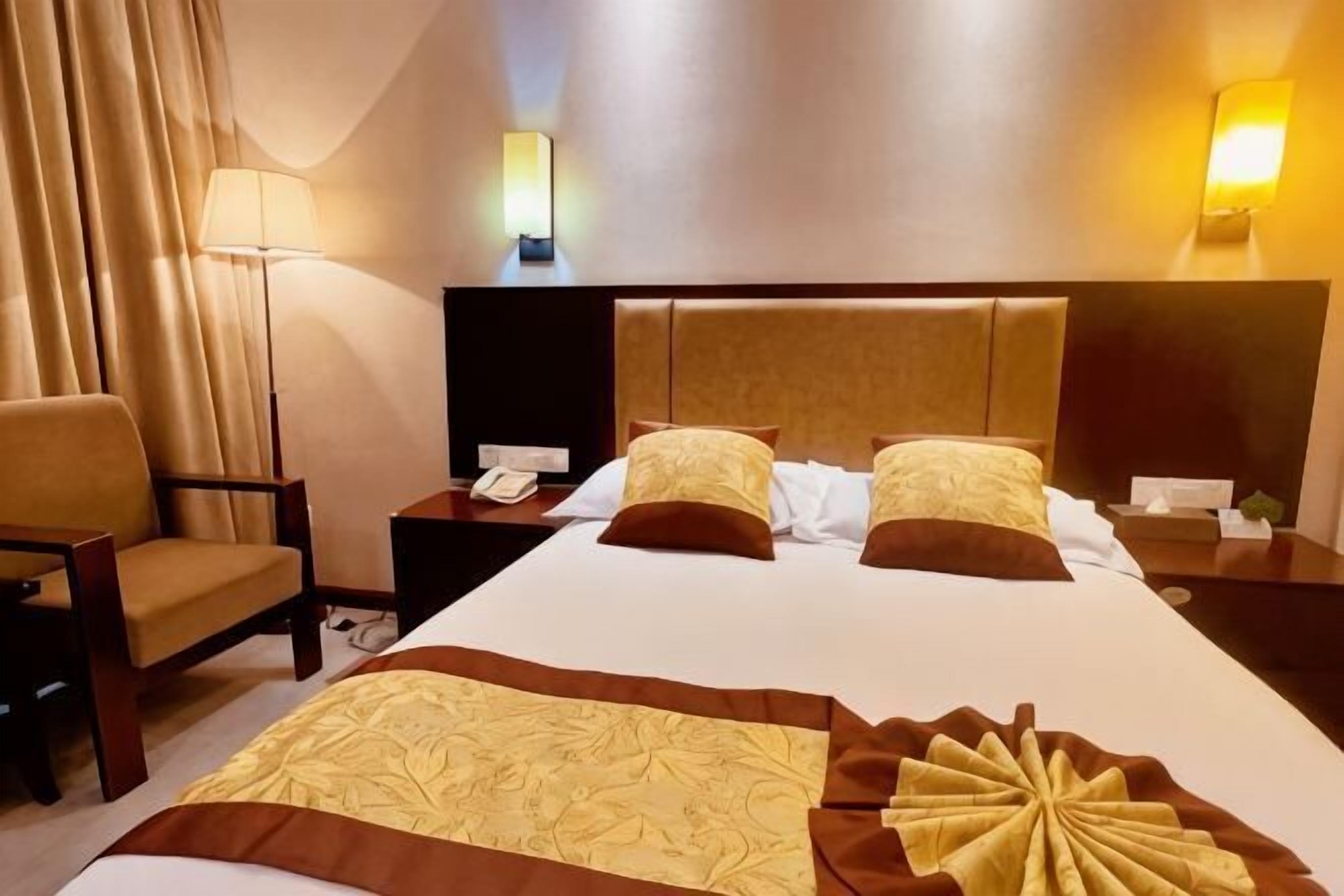 A hotel room with a large bed, two bedside tables, a chair, and a lamp.