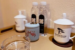 A table with a ceramic mug, a glass, a ceramic container, and two bottles. - Welcome Song Hotel (Huangshan City)