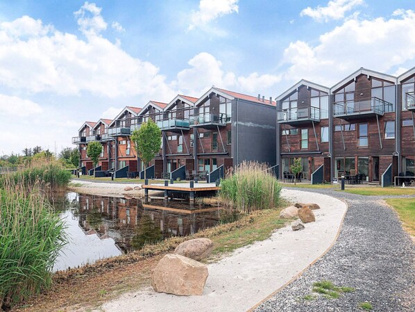 A modern residential building with multiple balconies, a small water feature, and a gravel path.