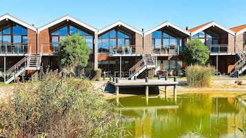 A row of modern, multi-story buildings with balconies, a dock, and a pond.