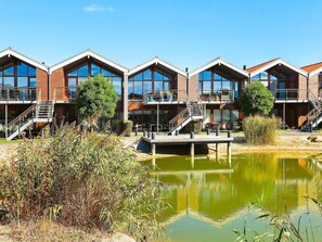 A row of modern, multi-story buildings with balconies, a dock, and a pond.