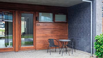 Un edificio con fachada de madera, puerta de vidrio y un pequeño espacio exterior con dos sillas y una mesa.
