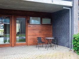 A building with a wooden facade, a glass door, and a small outdoor seating area with two chairs and a table.