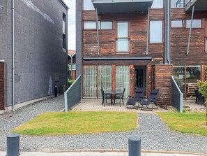 A modern building with a mix of brick and wooden facades, a covered outdoor seating area with tables and chairs, and a gravel pathway.