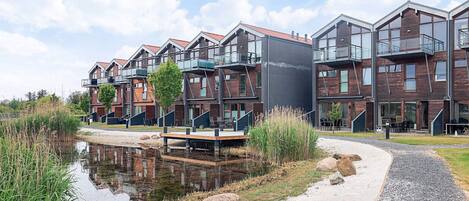 A modern residential complex with multiple buildings, a reflective water body, and a gravel path.