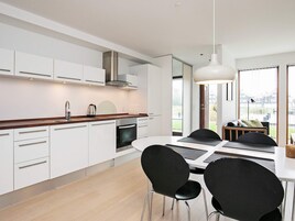 A modern kitchen with white cabinets, a stainless steel range hood, and a dining area with a white table and black chairs.