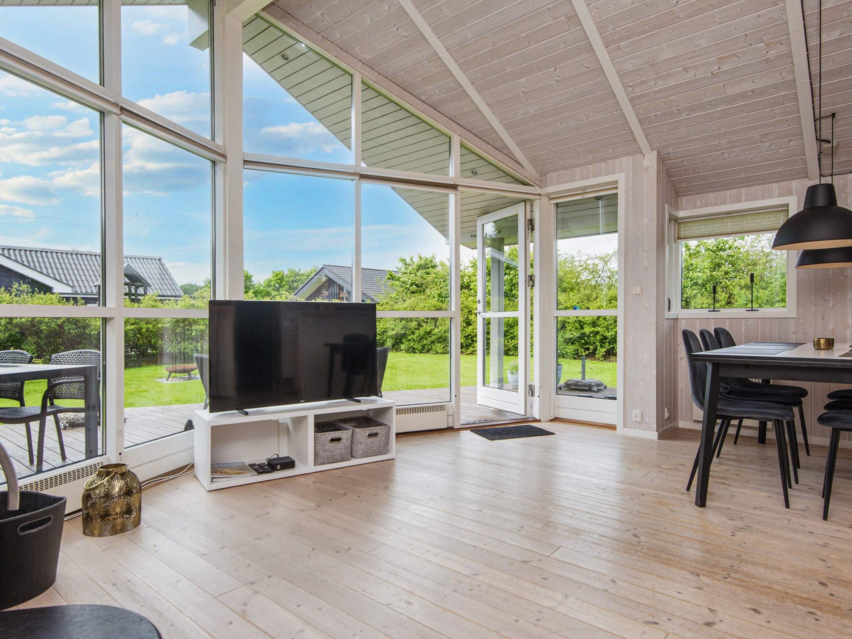 Ruime kamer met een grote televisie, houten vloeren en uitzicht op een tuin door grote ramen.