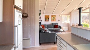 A modern kitchen with a built-in stove, a dining area with a grey sofa, and a wooden floor. - 6 Person Holiday Home in Juelsminde (Horsens)