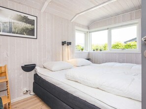 A bedroom with a bed, a desk, a chair, a window, and a wall-mounted shelf.