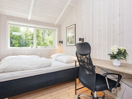 Un dormitorio con cama, escritorio, silla, ventana y una planta.