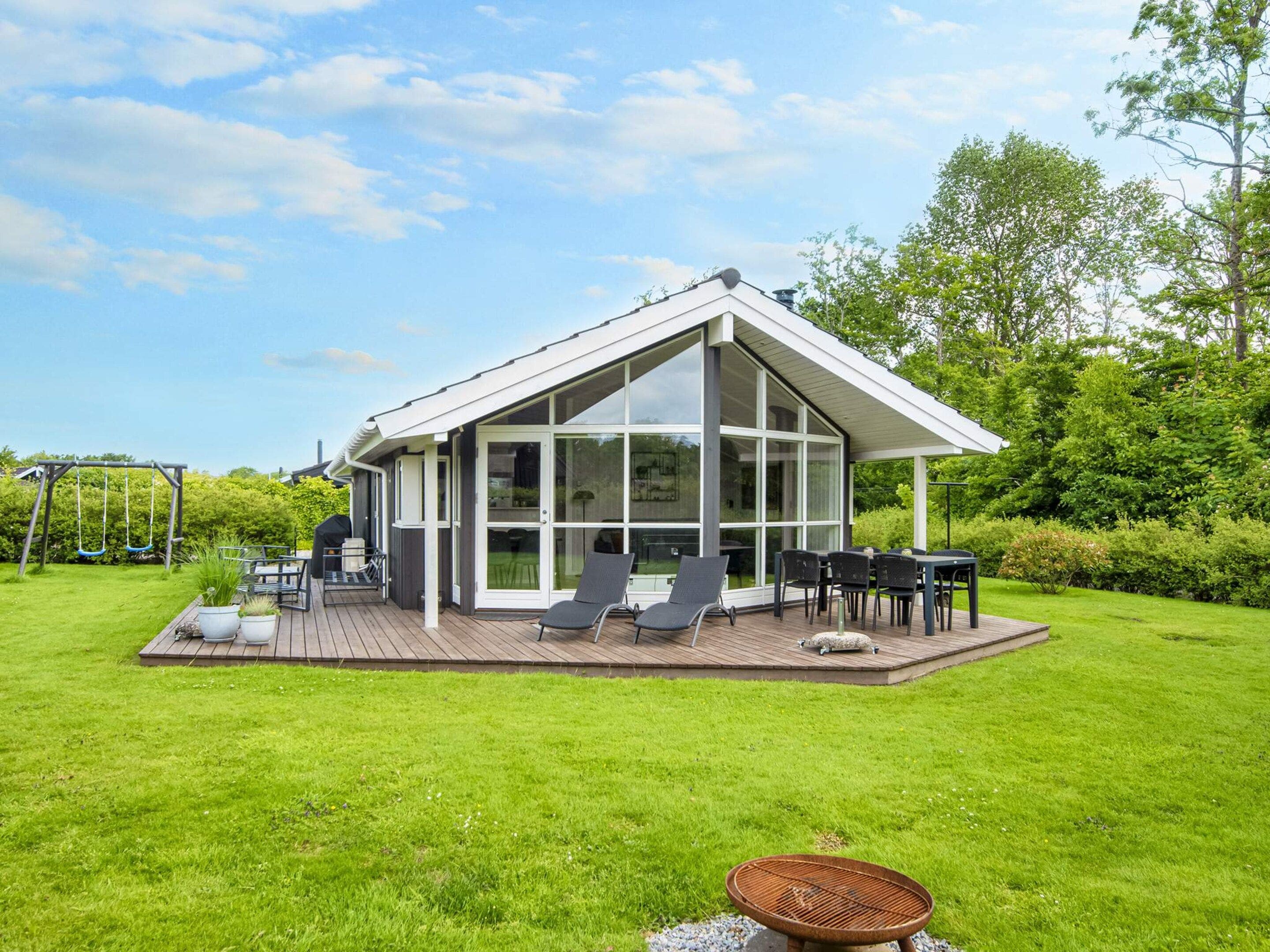 A modern house with a glass-enclosed patio, outdoor seating, and a swing set.
