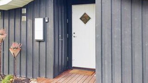 A building with a dark exterior, a white door with a diamond-shaped window, and a small white sign on the wall. - 6 Person Holiday Home in Juelsminde (Horsens)