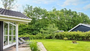 A wooden deck with outdoor furniture, a potted plant, and a small garden area with a lawn and trees. - 6 Person Holiday Home in Juelsminde (Horsens)