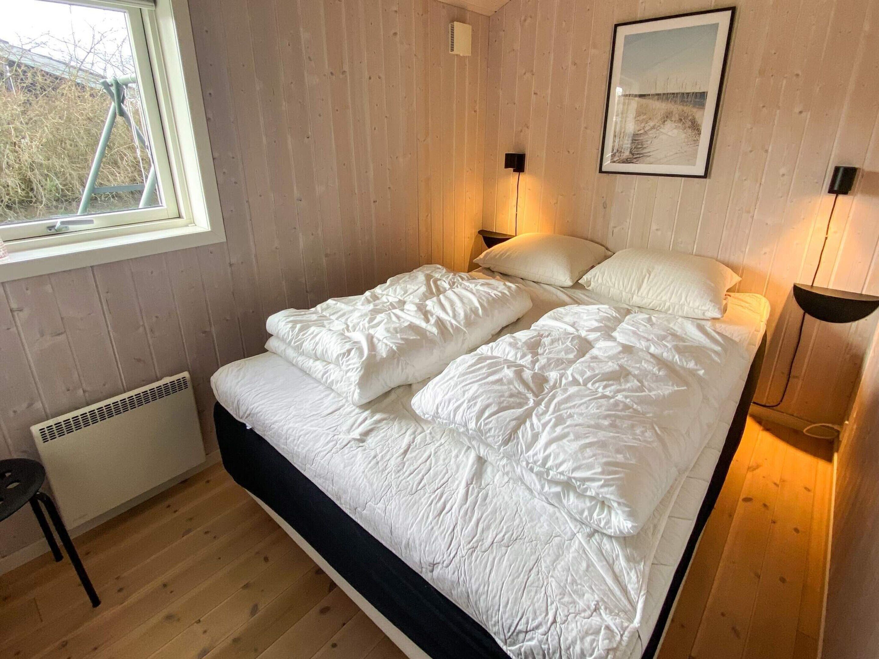 A bedroom with a bed, a window, a radiator, a chair, and a picture on the wall.