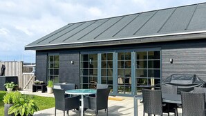 A modern building with a dark exterior, large glass doors, and outdoor seating area with wicker furniture. - 6 Person Holiday Home in Logstor (Logstor)