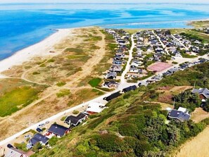 An aerial view of a coastal residential area with houses, a beach, and a road.