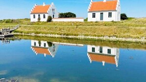 Two white buildings with orange roofs, a calm water body reflecting them, and a clear blue sky. - 6 Person Holiday Home in Logstor (Logstor)
