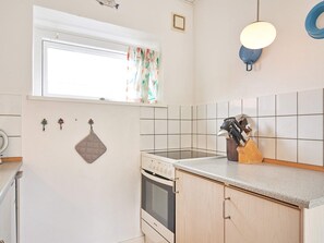A kitchen with a window, a stove, and a countertop with kitchen utensils. - 2 Person Holiday Home in Aakirkeby (Akirkeby)
