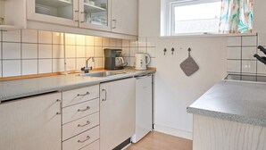 A kitchen with white cabinets, a countertop, a coffee maker, and a window with curtains. - 2 Person Holiday Home in Aakirkeby (Akirkeby)