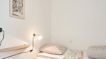 Un dormitorio con una cama individual, una lámpara de noche, una estantería en la pared y un cuadro enmarcado.