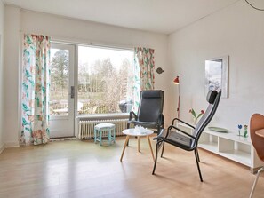 A room with a large window, a radiator, a black chair, a small stool, and a white table. - 2 Person Holiday Home in Aakirkeby (Akirkeby)
