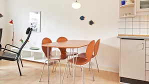 A modern kitchen with a round table and chairs, a hanging light fixture, and a tiled backsplash. - 2 Person Holiday Home in Aakirkeby (Akirkeby)